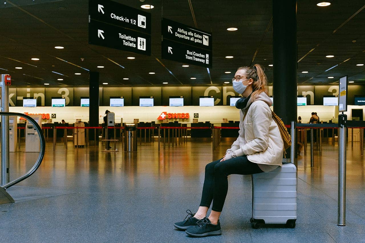 traveller with mask sitting on suitcase in airport