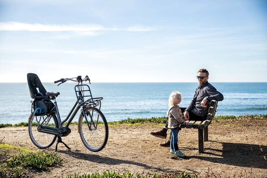 Man and child on bench by sea near their e-bike